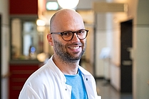 Mann mit Brille im weißen Kittel auf einem Krankenhausflur