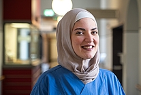 Porträt einer Frau mit buntem Kopftuch und blauem Kasack auf einem Krankenhausflur
